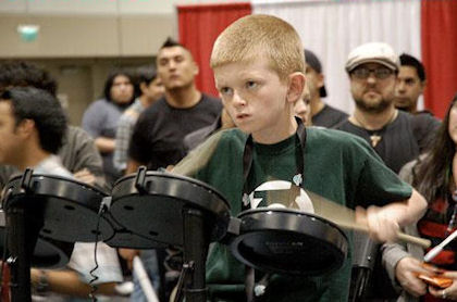 　DC Comicsのグリーン・ランタン コープスのシャツを着ている少年がゲーム「Rock Band」をプレーしている。