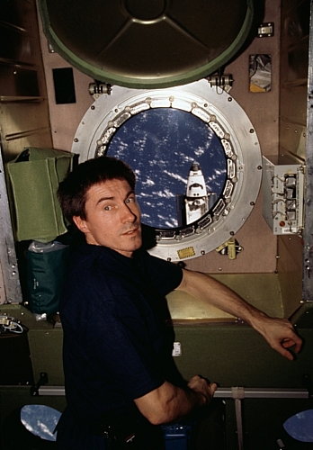 　ISSのZvezdaサービスモジュールに設けられた舷窓の前に座るSergei Krikalev氏。2001年2月に、スペースシャトルAtlantisが2機の乗組員による数日間の共同活動を行うために接近しているときに撮影された。この舷窓から、Atlantisの前部と乗組員室、そして西太平洋上空に点在する雲が見える。