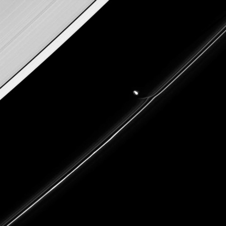 　土星衛星の1つプロメテウスが軌道周回中にF環を通過しているところ。プロメテウスは自身に向かってF環からの物質の流れをかすかに引きずっている。