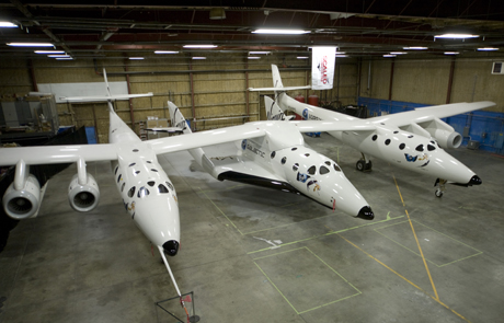 　格納庫で母船「VMS Eve」に取り付けられたSpaceShipTwo。VMS Eveは、SpaceShipTwoを地上5万フィート（約15.24km）まで運んだ後に切り離す。その後、SpaceShipTwoはロケットエンジンに点火して飛行を続ける。
