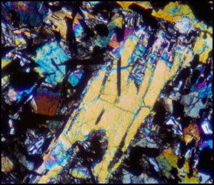 　月からの試料の顕微鏡写真。NASAはこの色の構成を次のように説明している。「水色と白色の鉱物は斜長石で、黒色のものはチタン鉄鉱。青色、緑色、オレンジ色、黄色、赤色に見えるものは輝石。大きい輝石は斑晶で、部分的に再吸収されている」