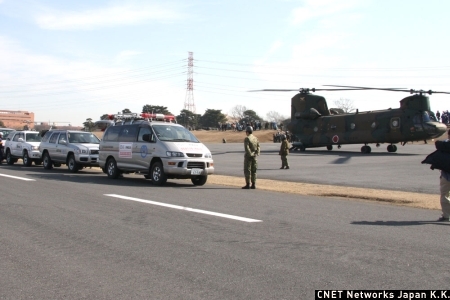 　今回の訓練では、避難場所の代々木公園への陸路が遮断されたことが判明し、ヘリコプターによる災害対策機器などの空輸を陸自に依頼するところから始まる。陸自はヘリコプター「CH-47J」や「UH-1J」を派遣。災害対策機器を搭載し、避難場所へ搬送する。写真は物資搬送に駆けつけた「CH-47J」（奥）と、被災地へ搬送する通信機材を搭載したNTTの車両（手前）だ。