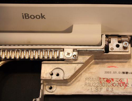 　液晶ディスプレイを取り外すには、複数のねじをiBookのシャーシから外す必要がある。さらにこの写真では、iBook内部から外部へ熱を逃がす金属製のヒートシンクブレードを確認できる（iBookの文字の下）。ヒートシンクの目的は、ロジックボードからの熱を逃がすことと、放熱パッドで発熱部品からの熱を逃がすことだ。