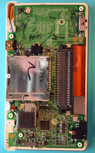 　底面のプラスチックケースを外すと、DL Liteの回路基板がはっきりと見える。中央右にあるのが周辺機器や「ゲームボーイアドバンス（GBA）」専用カートリッジを挿入するポート。中央左は、DS専用カードを挿入するポート。カード用ポートの下にはDS LiteのCPUがある。しかし、ポートを基板から取り外すにははんだごてが必要だ。