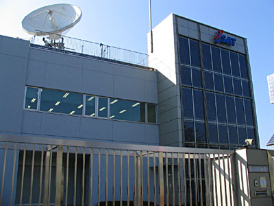 　SKY PerfecTV!やCATVの放送などを支えている施設が、神奈川県横浜市にある。それは、JR横浜線中山駅近くにあるJSATの横浜衛星管制センター（YSCC）だ。JSATは、アジア太平洋地域において最大規模の衛星通信事業者で、バックアップ衛星1機を含み、8軌道に9機の衛星を保有する。YSCCは、その通信衛星の管制業務を1年365日24時間、総勢およそ120名のスタッフが3交代制で行っている。写真は2004年に完成した新局舎のテレポート。