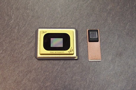 　Texas Instruments（TI）は、現在フロリダ州で開催中の「CTIA Wireless 2007」トレードショーにて、同社のデジタルライトプロセシング（DLP）技術をベースとした「超小型」プロジェクタの公開デモを実施している。同製品は、携帯電話に収まるほどの小さなビデオプロジェクタだ。左は、大画面テレビ等に搭載されている標準的なDLPチップ。右は、プロジェクタを搭載する携帯電話向けのDLPチップ。右のチップでもサイズは小さいが、かなり大きな画像を投影することができる。TIは、これらのチップを携帯電話に搭載することで、携帯電話を使用してより快適にビデオを見ることができるようにするとともに、当然ながら、より多くのチップの販売を狙っている。