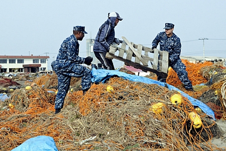 　三沢漁港で瓦礫を片付ける日本人男性を手助けする米海軍John Dicola二等兵曹とShakir Briggs一等兵曹（2011年3月14日撮影）。