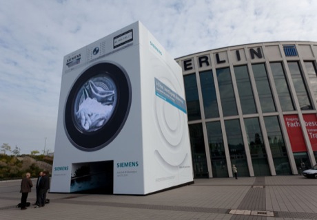 　IFAは家電だけの展示会ではないが、現在注目を集めているのはこの分野だ。家電製品はハイテク化の一途をたどっており、使用する電力と水量の少ない洗濯機や、究極のレモン絞り器、コーヒーメーカー、空気清浄機など、家電メーカー各社は製品開発にしのぎを削っている。写真はIFA会場であるMesse Berlinの南口で、Siemensが建物3階分の巨大な洗濯機を展示している。