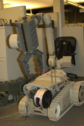 　iRobotの最大かつ最強の軍事用ロボットは、「iRobot Warrior」だ。220ポンド（約100kg）を持ち上げられるWarriorは、重たいものを持ち上げたり、引っ張ったりする必要がある任務をこなすことができる。Warriorロボットの初期版は、放射能計測器と工業用掃除機を搭載して、福島の原子力発電所における清掃作業を支援するために日本に送られた。2012年になって、ある原子力発電所事業者がWarriorを2台購入している。右側に見える光ファイバのスプールはワイヤレスネットワーク接続の代わりに使うためのものだ。