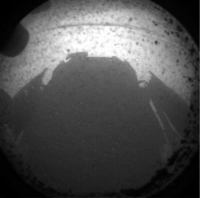 　2011年11月に打ち上げられた「Mars Science Laboratory」、つまり「Curiosity」と呼ばれる大型探査機は、ケネディ宇宙センターから3億5200万マイル（約5億6700万km）を飛行し、火星に到着した。着陸時刻は米国太平洋時間8月5日の午後10時を少し回った頃だった。

　この写真は、Curiosityから最初に地球へ送られた画像の1枚で、火星の地表に映った自機の影が撮影されている。米航空宇宙局（NASA）によると、透明のダストカバーがまだカメラに被せられているため、魚眼レンズで撮影された画像の縁に埃が映っているという。この写真は、機体前部に設置された、同探査機の前部危険回避カメラの1台によって、フル解像度の4分の1の解像度で撮影された。

　より大きなカラー画像は、Curiosityのマストが配備される今週中に送られてくるはずだ。マストには、より解像度の高いカメラが搭載されている。
