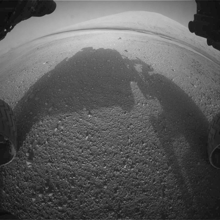 　Curiosity前部の危険回避カメラ（「hazcam」）が撮影したこの写真では、ゲイルクレーターの底からの高さが5.5kmあるシャープ山が南東方向に映っており、前景には自機が影を落としている。Curiosityの今後2年間のミッションは、まず着陸した地域の探査を行い、その後、シャープ山の側面を登って炭素化合物を探し、かつて火星に生物が生存可能な時期があったのかどうかを知る手がかりを得ることだ。