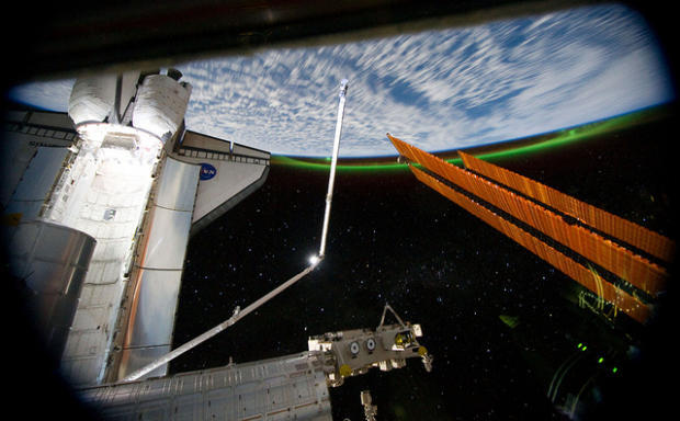 　このパノラマ写真では、スペースシャトルAtlantisが国際宇宙ステーションの太陽電池アレイの正面に見えており、地球は後方にある。さらに南極のオーロラも見える。