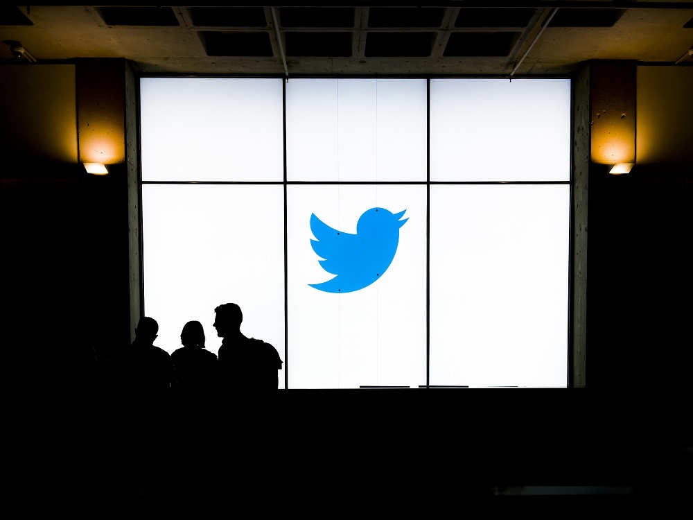 Twitterのロゴが掲示されている壁の前で話し合う人物たち