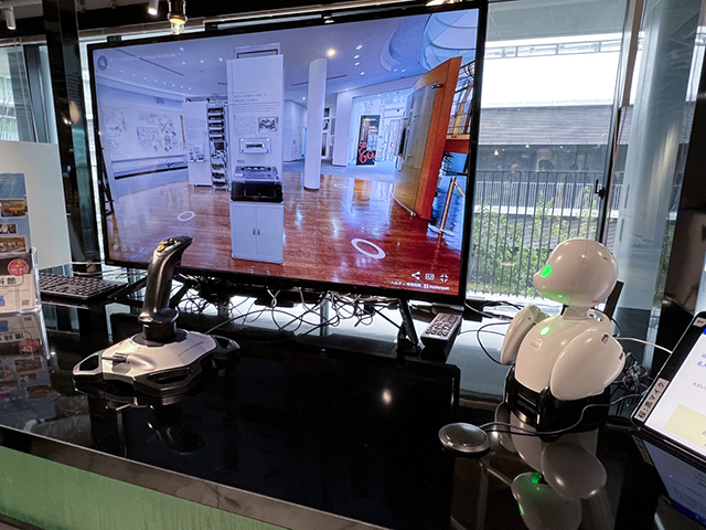 　東京の武蔵野市にあるNTT技術史料館の内部をジョイスティックで操作しながらツアーできるシステム。遠隔にいるスタッフが「OriHime」ロボットを通じて案内をしてくれる。
