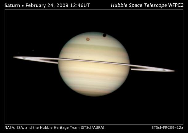　Hubble望遠鏡は、土星を公転する特に大きな衛星のうち4つが土星の前面を同時に横切る様子を記録した。極北に影を落としているオレンジ色の衛星がタイタンで、土星の環に近いのがミマス、左の方に見える明るい方の衛星がディオネ、淡い方の衛星がエンケラドゥスだ。