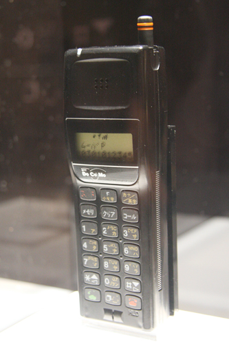 　1991年に登場した「ムーバP」。1989年当時、「世界で一番小型の携帯電話を作れ」との指令のもと、開発が開始された。ちょうど、世界中で携帯電話の小型化への競争が激しくなった頃だ。そして出来上がったのが体積100〜150ccの小型端末。それまで900点ほどあった部品が400点ほどまで削減され、部品の厚さは4mm程度に抑えられた。実はこのころに、それまでのNTTでは考えられなかったことが起こる。それがメーカー主導の開発だ。これ以降、メーカーによってデザインが異なってくるようになったのだ。
