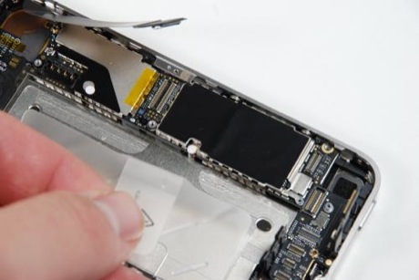 　iPhone 4のロジックボードを筐体から引き出すには、もう1つねじを取り外す必要がある。このねじは、黒い金属シールドの下にある、角が円形の小さな白いステッカーで隠されている。