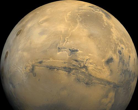 　「Viking 1号Orbiter」が1980年2月22日に軌道1334から撮影した、102枚の火星画像の全球モザイク写真。撮影された画像は、点透視投影を行い、高度2500kmに位置する宇宙船から見た状態を表している。

　中心にあるのはマリネリス渓谷で、長さ3000km以上、深さは最大8kmだ。マリネリス渓谷の中心および東側の位置から、右上の暗いアキダリア平原に向かって、上方（北）へ溝が走っている。左側にあるのは、タルシス山地の3つの火山で、南側には、過去に大きな衝突があった地帯がある（Viking 1号Orbiter、MG07S078-334SP）。
