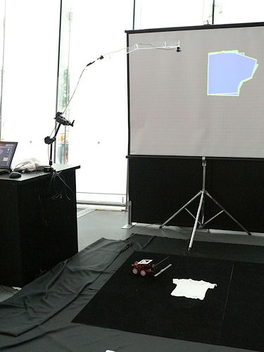 　コンピュータグラフィックス（CG）やバーチャルリアリティ（VR）といったデジタルコンテンツ技術をもとにしたメディアアートや研究物などが一堂に会するイベント「DIGITAL CONTENT EXPO 2009」。10月22日から10月25日まで東京の日本科学未来館および東京国際交流館で開催されている。見て、触れて楽しめる作品が数多く展示されている同イベントから、一部を写真で紹介する。

　こちらは独立行政法人科学技術振興機構（JST）五十嵐デザインインターフェースプロジェクトの「Foldy」。PC上で自分好みの服のたたみ方を入力すると、ロボットがそれを実行してくれるというもの。上部に伸びるカメラが服やロボットを認識する。