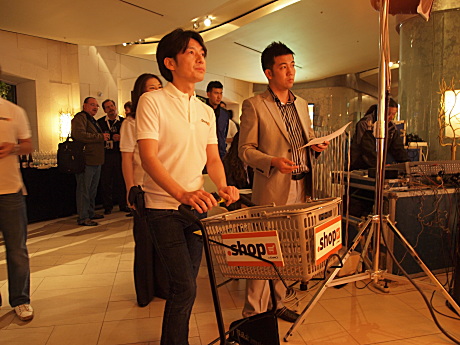 　「.shop」のイメージにあわせ、GMOインターネット代表取締役会長兼社長 グループ代表の熊谷正寿はショッピングカートを引いてスピーチに登場。買い物かごを手に話した。