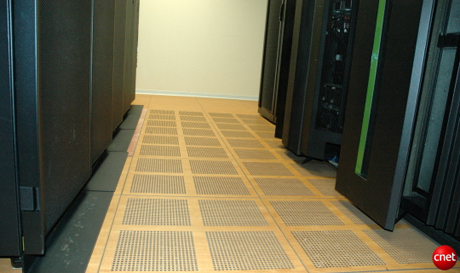 　IBMの「グリーンな」データセンターは、冷却システムを最適化するような空気の流れを生み出すように設計されている。冷気は、この上げ床の下からポンプで引き込まれ、サーバおよびストレージシステムの前面へ流れる。こうした「冷気通路」と交互に設置されているのが「暖気通路」で、そこではサーバやストレージのラックの背面が向かい合っている。暖気通路には、天井の上に暖気を排出するための通気孔がある。この施設では、種々雑多なケーブルを床下に押し込むのではなく、床下に通すのは電源コードだけ、ネットワークケーブルは上方にまとめるという配置にして、空気の流れを妨げないようにしている。