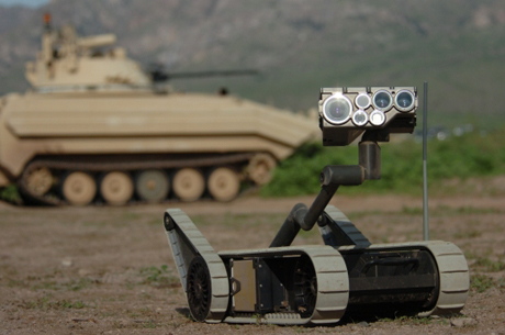 　手前に写っている小さなロボット君は、「WALL・E／ウォーリー」の役を逃したように見えるかもしれないが、実際には、米陸軍の長期構想である「Future Combat Systems（FCS）」の主役級だ。写真は、7月末のニューメキシコ州での演習に登場したときのもの。一部のやや未来的な兵器を戦闘に即応しうるものにするという陸軍の意向にともない、当初のFCSのスケジュールが前倒しされた。

　SUGV（小型無人地上車両）として知られるこのロボットを「やや未来的」と表現するのは、「iRobot PackBot」をはじめとする、すでにイラクなどの危険地帯で幅広く使われている遠隔操作で動く機器とさほど変わらないためだ。着手から5年ほど経つFCS構想が目指すさらに重要な未来は、2つの領域が鍵を握る。1つは、古い兵器、機器を21世紀のテクノロジに置き換えること。もう1つは、ロボット、センサ、榴弾砲といった多くのソフトウェアを利用したFCSと兵士をユビキタスな高速ワイヤレスネットワークでリンクすることだ。