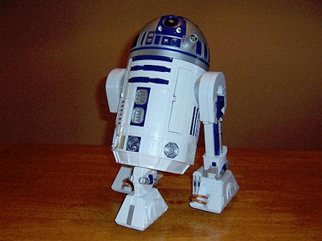 　今回は、おもちゃとは言え、驚くほどの機能を持つロボットを分解して、中にKenny Baker氏（映画「スター・ウォーズ」シリーズで「R2-D2」の内部に入っていた俳優）が入っていないことを確かめてみよう。おもちゃメーカー、Hasbroのインタラクティブロボット「R2-D2」は、スター・ウォーズに登場するロボット、R2-D2のレプリカで、高さはおよそ16インチ（約40cm）。光沢があって精巧な仕上がりで、大きさの比較対象になるものがない写真では本物と見間違えてしまうほど、よくできている。TechRepublicでは、このロボットが実際に動いている姿を動画で紹介している。このR2-D2には、ナビゲーションセンサ（物を「見る」超音波センサ）と赤外線位置センサ（動いている人間を探知する）が搭載されている。パッケージに書かれた説明によると、R2-D2は持ち主について回り、ダース・ベイダーが何者かを知っていて、さらには声で命令して飲み物を持ってくるように訓練できるなど、さまざまな機能を備えているという。そしてもちろん、本物と同じように、機嫌を損ねるとピーピーとお決まりの電子音を出す。R2-D2のドーム型の頭部の真下には音声認識モジュールがあり、胴体部分の中心には、効果音を出すスピーカーが入っている。2本の足には頑丈な車輪が2個ずつついていて、3本目の足には大きなトラックボールがついている。トラックボールがあるなんて変だと思うかもしれないが、このおかげでR2-D2は、厚手のカーペットの上もスイスイと移動できる。（CNET Networksの姉妹サイト、TechRepublicでは「分解レポート」シリーズを連載している。さまざまなガジェットを実際に分解して、内部をのぞいてみようという企画だ。CNET News.comでは、その一部を抜粋してお届けしている）