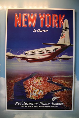 　Pan American World Airwaysのビンテージポスター「New York by Clipper」の複製品。4エンジンを搭載した飛行機がマンハッタンに南方から接近している。