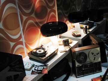 　オーディオビジュアル技術の大手企業であるTDKは9月の第1週から、ロンドンのコヴェント・ガーデンで、「Life on Record」トレーラーを公開し、自社の歴史を披露した。トレーラーでは、過去40年間に登場した有名なハードウェアとともに、同社のテクノロジが紹介された。

　この写真は、レコードプレーヤーとTDKのテープが使われているテープレコーダー。レトロなテーブルランプも一緒に写っている。