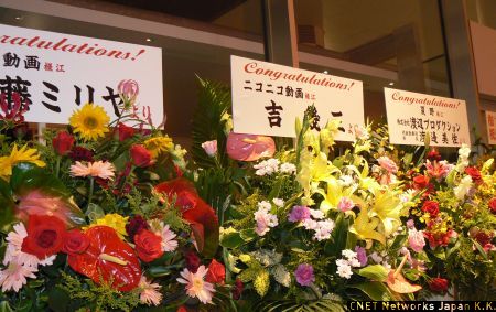 　会場には多くの花束が届いていた。そのうちのいくつかを紹介する。中でも注目を集めていたのは、ニコニコ動画内で「俺ら東京さ行ぐだ」をリミックスした楽曲が数多く作られ、「IKZO」と呼ばれて人気の吉幾三さんからの花束。多くの来場者が写真に収めていた。