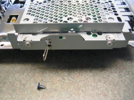 　ハードディスクを覆うケージ部分にある、1本だけ青色になっているネジを取り外す。引き起こし式のワイヤータブを引いてコネクタからハードディスクをスライドさせ、金属シールドの囲いからハードディスクのケージを外す。