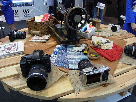 　オリンパスブースでは、複数のテーブルに最新のカメラが多数用意されている。小物など撮影用の被写体も置かれており、自由に撮影可能だ。2月8日に発売したばかりのコンパクトデジタルカメラや12月に発売した重量454gのマイクロ一眼「OLYMPUS PEN Lite E-PL1s」など多数のカメラが展示されている。