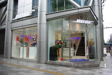 　ボーズは7月8日、日本国内で23店舗目となる直営店「ボーズ・プレミアムストア心斎橋」を大阪・心斎橋（大阪市中央区西心斎橋1-1-10 シエロ・アズールビルディング）にオープンする。場所は地下鉄心斎橋駅から徒歩約3分。周りには海外のファッションブランドが軒を連ねる。ボーズ初の大型路面店となるボーズ・プレミアムストアの店舗内を写真で紹介する。

　こちらは店舗入り口。1階にはヘッドホンやミュージックシステムなどのパーソナル製品、2階には本格的なホームシアタールームを備える。展示されているのは28製品37アイテム。コンシューマー向けのほぼすべての製品を実際に視聴でき、購入が可能だ。