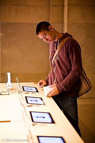 　Apple製品を並べた複数のテーブルが置かれている。その1つでiPadをチェックする男性。