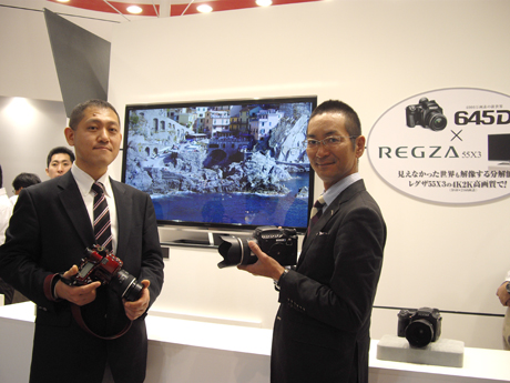 　ペンタックスリコーイメージングでは、約4000万の有効画素を持つ中判デジタル一眼レフカメラ「645D」を、東芝の4K2K解像度の55V型液晶テレビ「REGZA 55X3」を組み合わせて展示した。ペンタックスリコーイメージングのマーケティング統括部商品企画グループの前川泰之氏（左）と東芝デジタルプロダクツ＆サービス第一事業部国内企画・マーケティング部の本村裕史氏（右）。本村氏は4K画質を見て「リアリティそのもの。4Kテレビで写真を見るという楽しみ方が生まれ始めた」とコメントした。