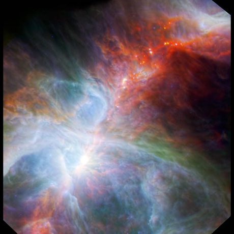 　この写真は、Spitzer宇宙望遠鏡のカメラからのデータを統合したもので、明るい若い星と、低温でちりが多い周囲のオリオン星雲の雲の相互作用を描いている。

　低温のガスが「トラペジウム」の間に赤くたなびいているのが見える。トラペジウムは、強烈な明るさの領域で、4個の青白い大質量星があり、星の多い領域になろうとしている。
