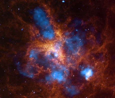 　この写真は、「かじき座30」の中心にある2400個もの大質量星で、物質を放出する際に強い放射と強力な恒星風を生み出している。Chandra X線望遠鏡がX線（青色）領域で検出した数百万度のガスは、こうした恒星風や超新星爆発で形成された衝撃波面で生じたものだ。この高温のガスは、周囲の低温のガスやちりの中に巨大な泡を作り出している。この泡は、このSpitzer宇宙望遠鏡の写真では赤外線のオレンジ色の部分にあたる。