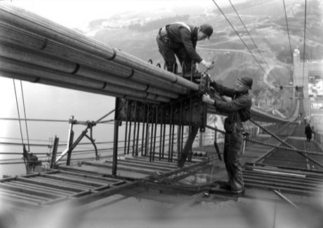 　この1936年の写真では、下方に見える湾のはるか上で、ゴールデンゲートブリッジの建設作業員らがメインケーブルの1本に対して作業を行っている。