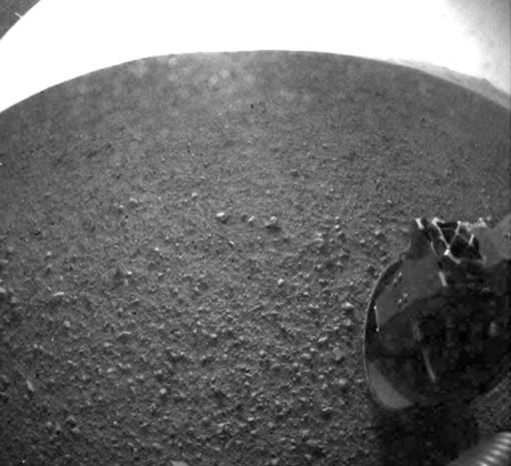 　これは、先ほどの画像の鮮明なバージョンだ。後部に搭載された危険回避カメラで撮影されたこの画像には、Curiosityの6つの車輪のうち1つ（右下）と電源の一部（左上）が映っている。NASAによると、撮影時にカメラがまっすぐ太陽の方に向けられていたため、画像の上部に光が入り込んでいるという。

　エンジニアたちは写真がすぐに送られてくるとは期待していなかったのだが、着陸後数分すると、解像度の低いぼやけたサムネイル写真が同探査機後部の危険回避カメラから送信され、火星地表に降り立った車輪を映し出していた。

　ミッションコントロールコメンテーターであるAllen Chen氏はこのように述べた。「『Odyssey』のデータは今も強力だ。Odysseyは良好な状態で、空の彼方にいる。今われわれは、画像が送られてくるのを待っているところだ」

　「サムネイル写真が届いた」と誰かが言った。

　「火星に着陸した」とChen氏は伝えた。
