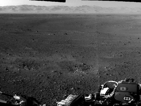 　米航空宇宙局（NASA）の探査機「Curiosity」は、細心の注意を要する見事な着陸を成し遂げ、世界中の膨大な数の人々がそれを目撃した。そのわずか数日後、Curiosityはマストに搭載された複数のナビゲーションカメラで撮影した火星表面の最初のフル解像度画像を地球に送った。

　Curiosityで最も高い位置にあるマストは、着陸後に展開された。そして、2台のナビゲーションカメラはミディアムアングルで45度の視野を有しており、火星の地形について3次元の情報を送ることができる。それらのカメラは風景を広範かつ迅速に調査できるように設計されており、辺り一面や上下を観察することが可能だ。

　ゲイルクレーターの小石の多いリムの近くで撮影されたこの画像の風景は、侵食のために非常に山が多くなっており、中景は低く起伏する傾斜面と平地で構成されている。前景には、おそらくCuriosityの下降段スラスタの爆風で掘り起こされたのであろう2つのはっきりとしたくぼみが写っている。

　1024×1024ピクセルのフル解像度画像はこちらで見ることができる。
