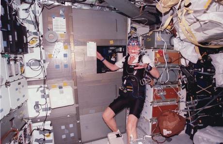 　睡眠モニタリング装置を体中に付け、自分のスリープステーションのそばに立つJohn Glenn氏。1998年に、地球周回軌道上のスペースシャトルDiscoveryのミッドデッキで撮影した。

　乗り物酔いなどの症状や、宇宙にいるという興奮だけでも、宇宙飛行士の睡眠パターンを乱す原因になる可能性がある。睡眠用の設備は狭く、すぐにほかの人の様子が聞こえてしまう。さらにミッション中は、90分に1回という頻度で日の出がやって来る。宇宙飛行士の中には、窓越しに差し込む太陽光線が目に入らないようにアイマスクを使う人もいる。
