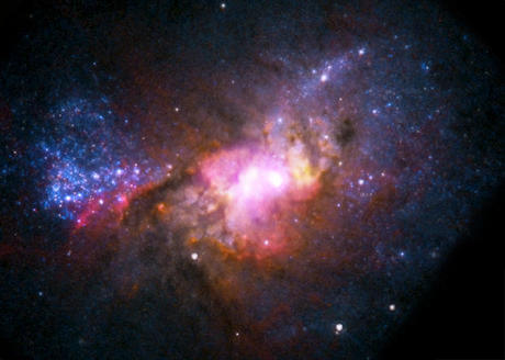 　この画像では、Hubble宇宙望遠鏡からの可視光データが赤色、緑色、青色、NASAのChandra X線観測衛星からのX線データが紫色、米国立電波天文台（NRAO）の超大型電波干渉計（Very Large Array：VLA）からの電波データが黄色で、それぞれ示されている。銀河の中心にあるコンパクトX線源が電波源と一致している。これは、太陽の約100万倍の質量を持つ超大質量ブラックホールが活発に成長していることを示す証拠だ。

　複数の望遠鏡を使って「Henize 2-10（地球から約3000万光年の距離にある矮小スターバースト銀河）」を観測することにより、天文学者は、初期宇宙で銀河とブラックホールの形成がどのようにして起きたのかを詳しく調べることができる。
