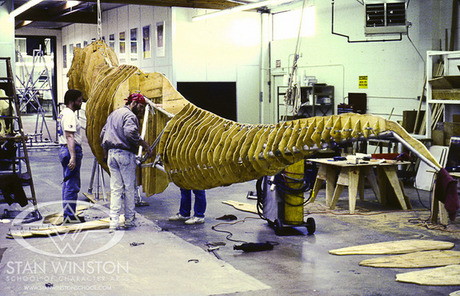 　高さ20フィート（約6m）、体長40フィート（約12m）のリアルなティラノサウルスを作るために、アニマトロニクスの第一人者であるRichard Davison氏とAlan Scott氏は、アルミニウムのフレームに合板をいくつも取り付けている。ここから、作業者たちが金網を巻き、全体を液体のファイバーグラスで固め、その上から3トンもの油粘土を付けていく。