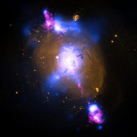 　X線データと光学データ、電波データを組み合わせて、天文学者たちは銀河「4C+29.30」の中心にある巨大ブラックホールの全貌を知ることができた。画像の中心近くで確認できるChandraのX線データ（青色で示されている）は、ブラックホール周辺にたまった数百万度のガスを表している。Hubbleが観測した光学データは金色、米国立科学財団（NSF）の超大型干渉電波望遠鏡群（VLA）からの電波はピンク色で示されている。