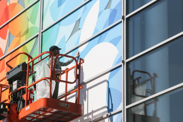 　作業員が会場正面のガラスにAppleの大きな白いロゴを貼り付けている。
