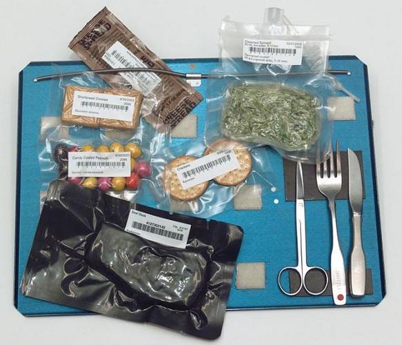 　宇宙ステーションでの食事は上等というわけではない。ここに写っているのは、（ナイフやフォークなどの）食事用の器具とともに、1人分に小分けされたフリーズドライ加工の宇宙食パックの数々だ。これらのパックは面ファスナーでトレーに貼り付けられている。