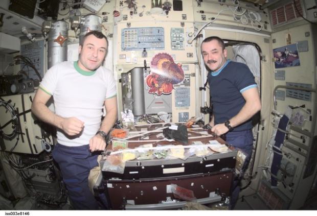 　2001年11月22日、Vladimir N. Dezhurov宇宙飛行士（左）とTyurin宇宙飛行士がISSのZvezda Service Moduleで感謝祭の食事をしている様子。2人はいずれもExpedition 3のフライトエンジニアであり、ロシア連邦宇宙局を代表している。