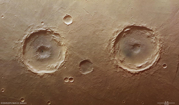 　この写真は、火星のマリネリス峡谷のすぐ南にあるタウマシア平原の自然色画像で、直径約50kmのクレーターが2つ写っている。