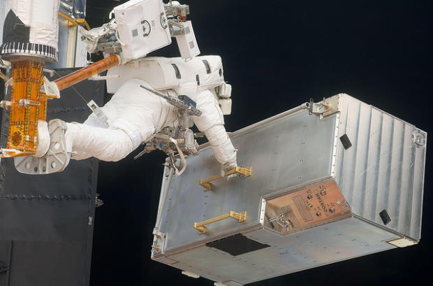 　2009年撮影のこの写真では、Andrew Feustel宇宙飛行士が、スペースシャトル「Atlantis」のロボットアームの先端にある足場を使って、「Hubble」宇宙望遠鏡の改修作業に使われる部品を移動させている。