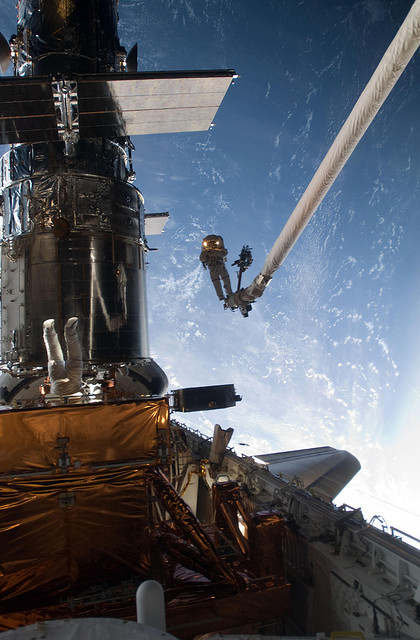 　John Grunsfeld宇宙飛行士が、スペースシャトル「Atlantis」のロボットアームの先端にある足場に立っている。